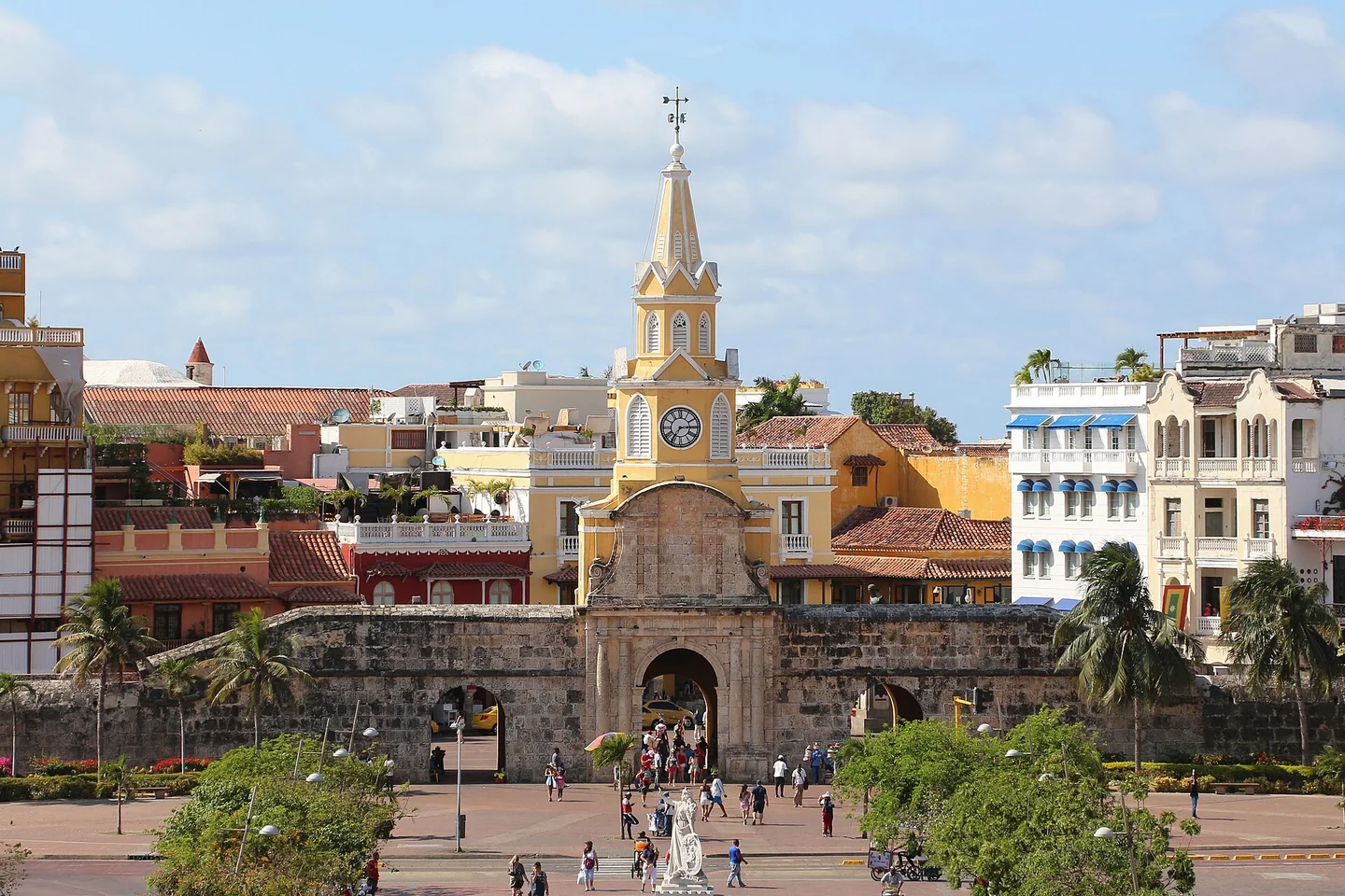 La Torre del Reloj amarilla y la histórica puerta de piedra de Cartagena se alzan sobre la plaza y los edificios coloridos del centro histórico.