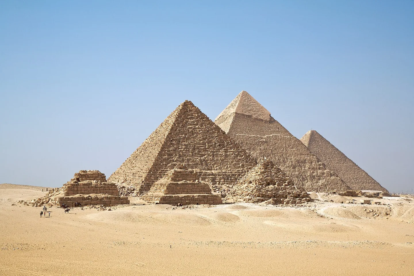 The pyramids of Giza rise from golden desert sand beneath a clear blue sky.