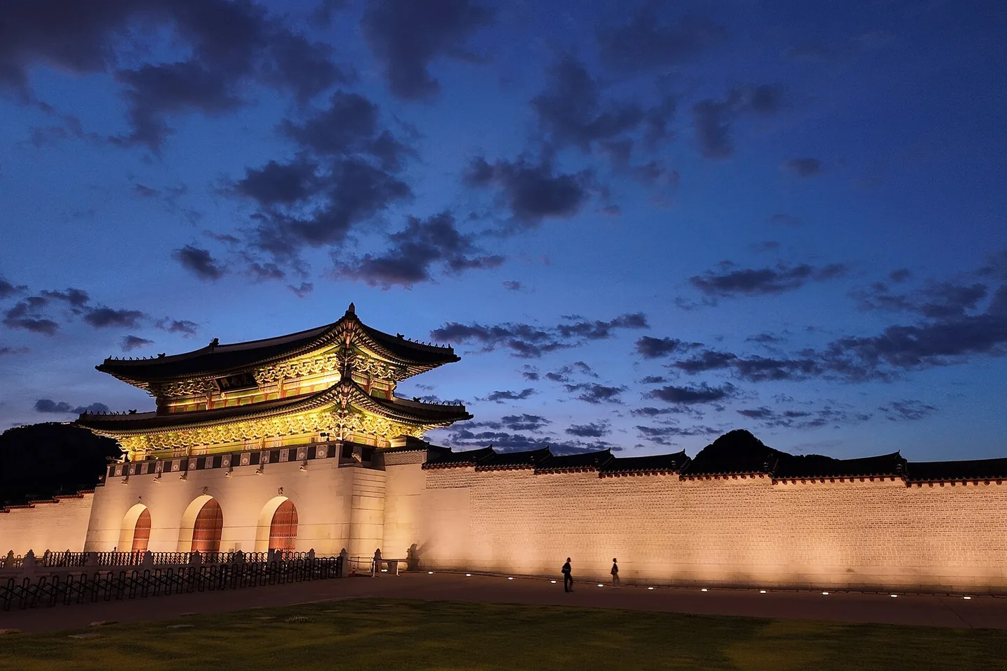 The illuminated gate of Gyeongbokgung Palace under a blue evening sky in Seoul.