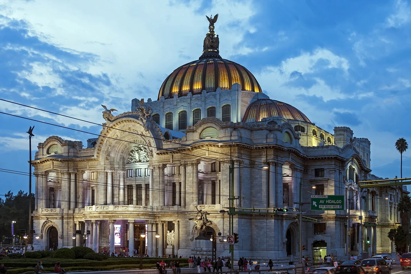The illuminated marble façade and golden dome of the Palacio de Bellas Artes beneath a blue evening sky in Mexico City.