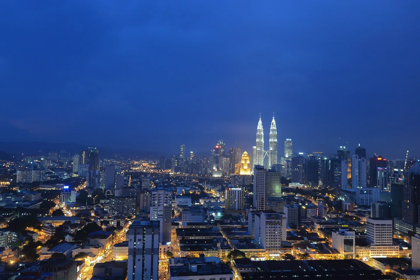 The Petronas Twin Towers rise above Kuala Lumpur's illuminated streets at blue hour.