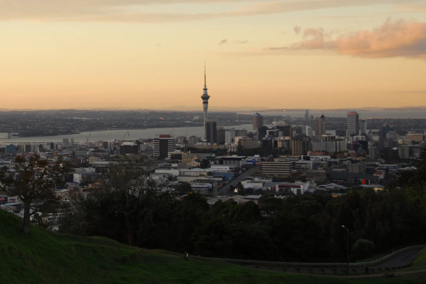 Auckland's Sky Tower rises above the city and harbor beneath a golden evening sky, seen from Mount Eden.