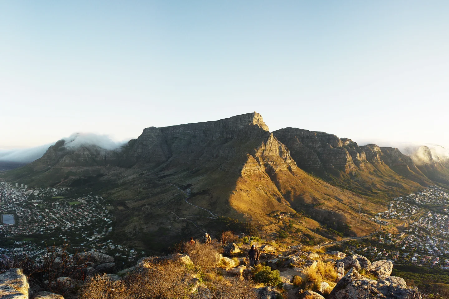 Table Mountain's flat summit rises above Cape Town in warm light, with clouds spilling over its slopes.